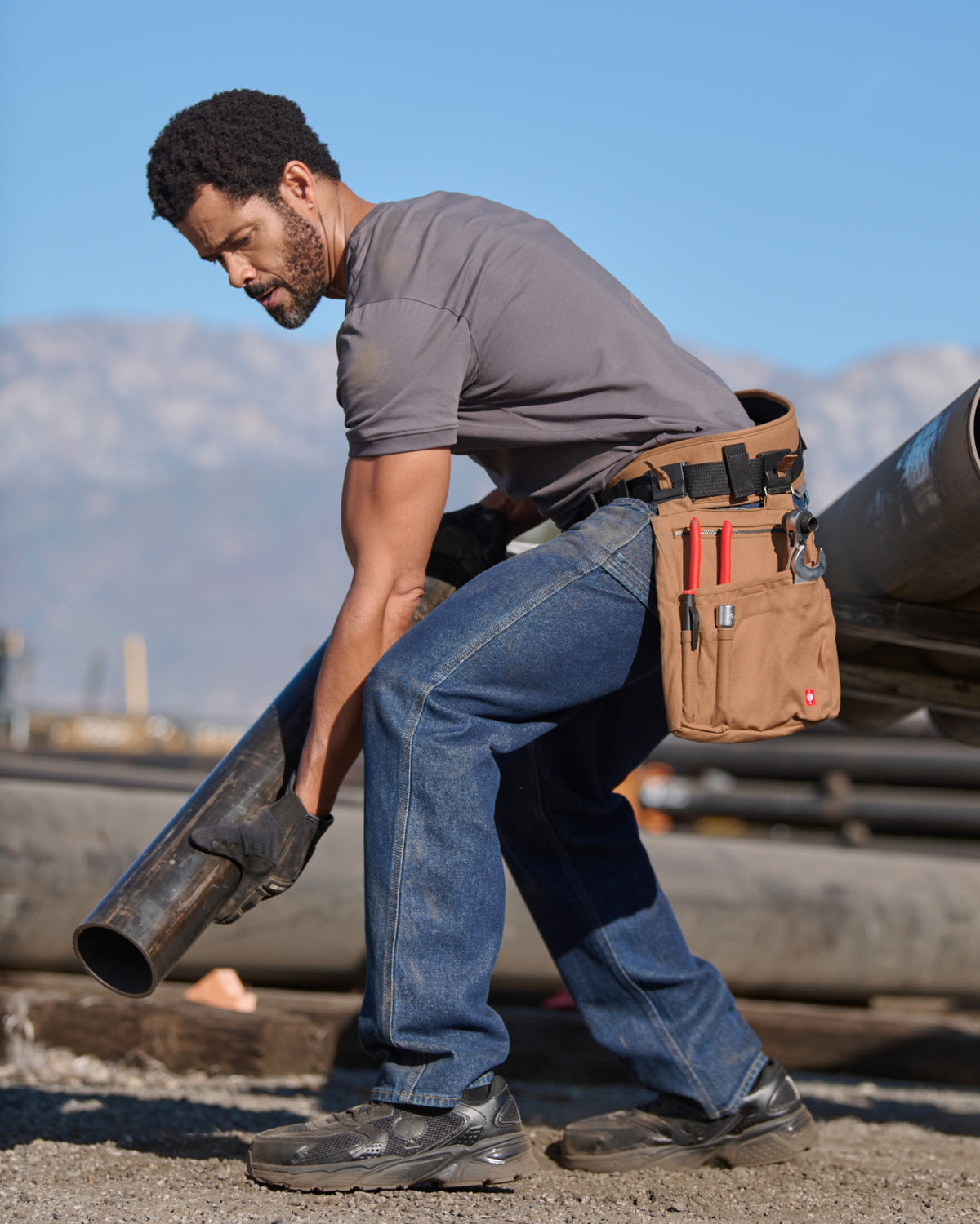 A almond brown STRAUSS e.s.iconic tool bag is fastened to work pants while a worker reaches for hand tools.