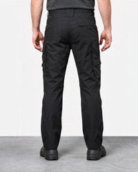 Rear view of a person wearing black cargo pants with side flap pockets and black shoes, standing against a plain light gray studio background.