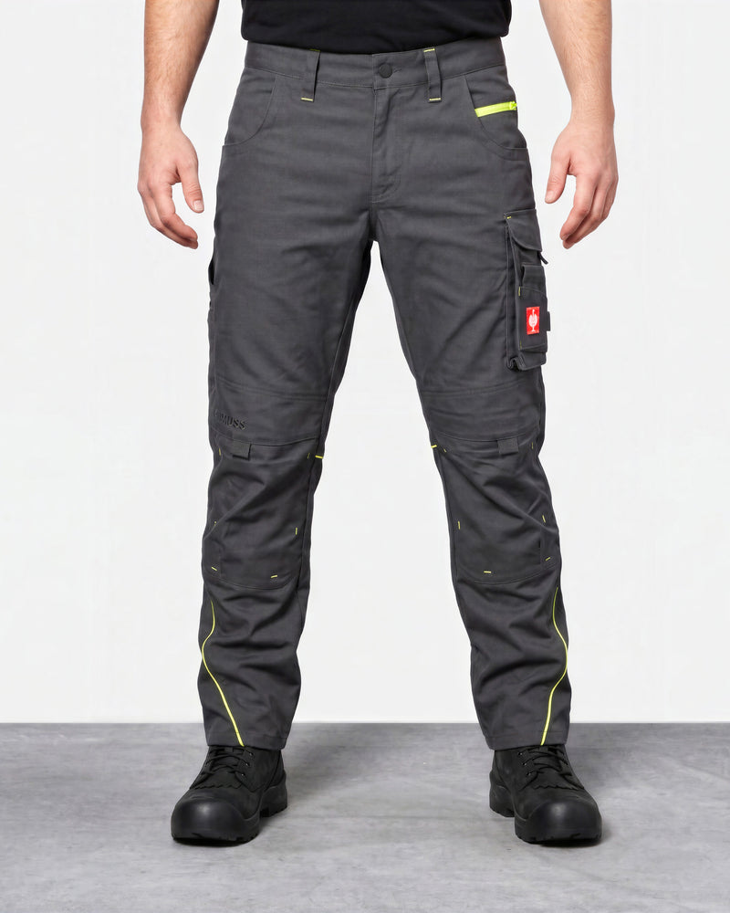 A person wearing dark gray work pants with bright yellow-green contrast stitching and a red brand tab on the cargo pocket, standing against a light gray studio background.