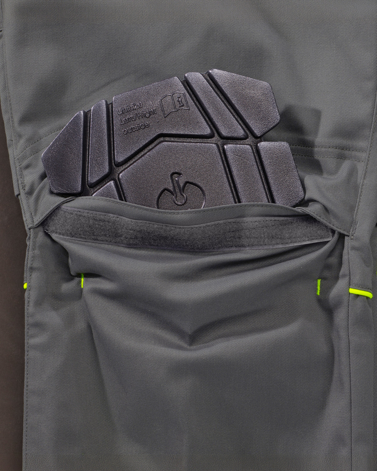 Close-up of a dark gray technical knee pad pocket showing a built-in protective pad with molded text and logo embossing.