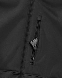 Close-up of a black jacket showing a vertical zippered pocket with a textured black pull tab.