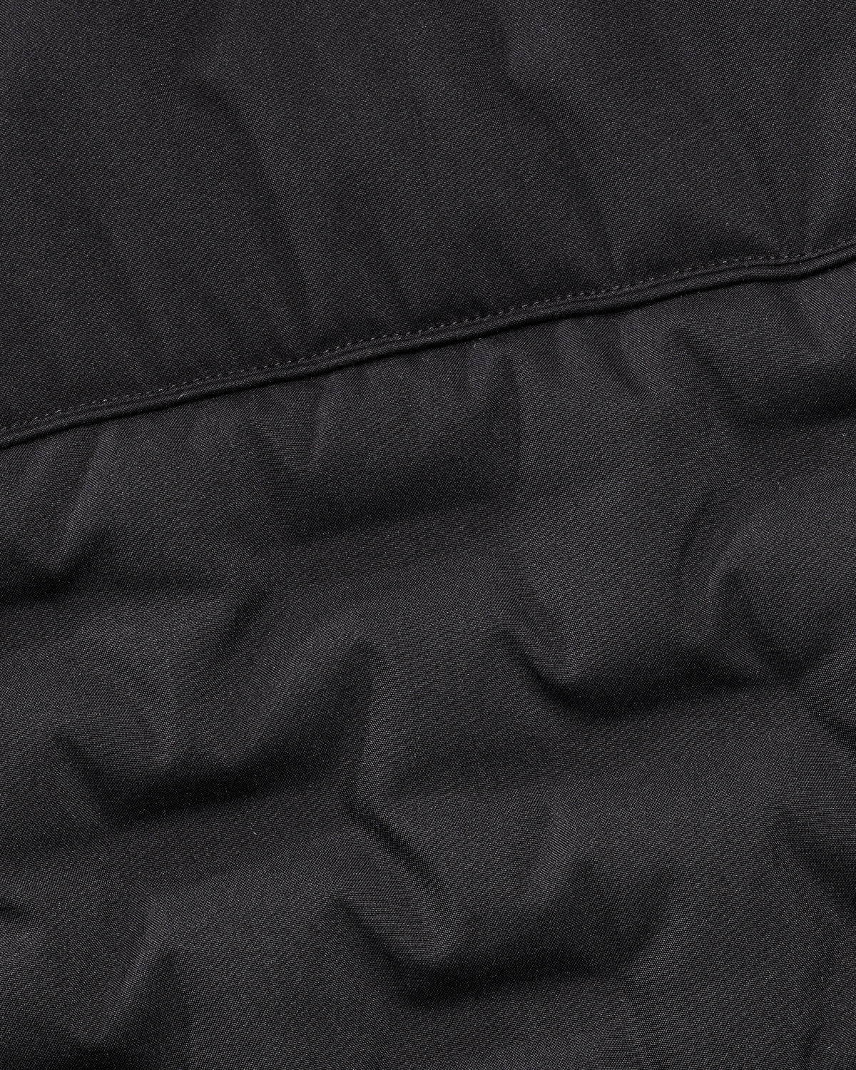 Close-up of a black quilted puffer jacket fabric showing the stitched panel construction.
