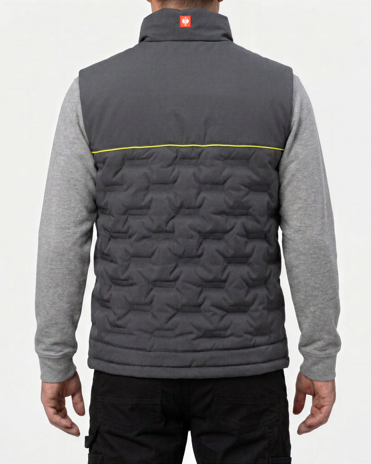 A man viewed from the back wearing a dark gray quilted vest over a heather gray long-sleeve shirt and black pants. The vest features a geometric star pattern, a high collar, and a thin yellow horizontal stripe across the upper back.