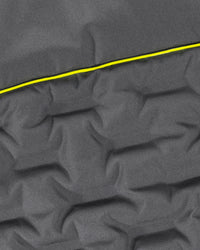 Close-up of dark gray quilted fabric with a bright yellow stitched line running diagonally across the surface.