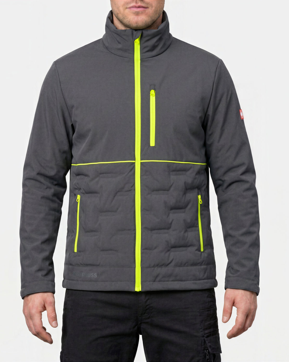 A man wearing a dark gray quilted jacket with bright neon yellow-green zipper accents, shown from the chin down against a light gray studio background.