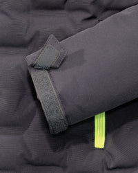 Close-up of a dark gray puffer jacket sleeve showing a hook-and-loop strap closure and a bright neon yellow zipper pull.