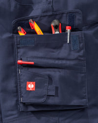 Close-up of a navy blue work pants pocket holding various hand tools, featuring a small red square patch with a white rooster logo on the front flap.