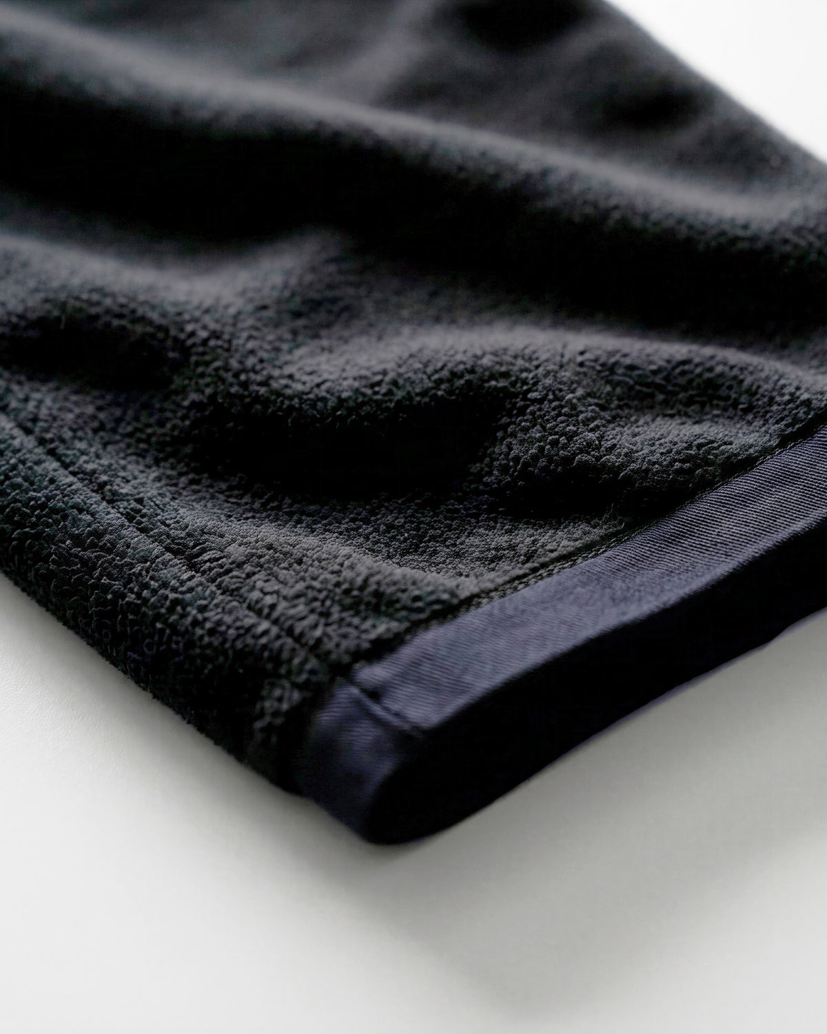 A close-up of a dark charcoal gray or black textured fabric, likely a towel or blanket, folded over on a clean white surface.