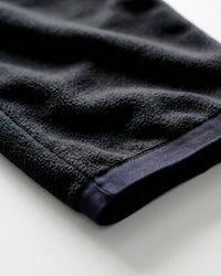 A close-up of a dark charcoal gray or black textured fabric, likely a towel or blanket, folded over on a clean white surface.