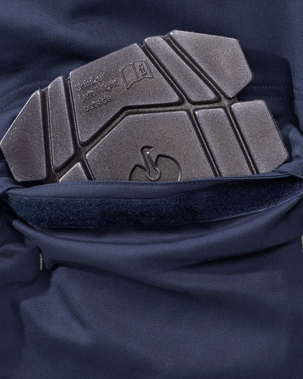 Close-up of a dark gray textured protective pad with embossed branding and text, attached to a navy blue fabric garment.