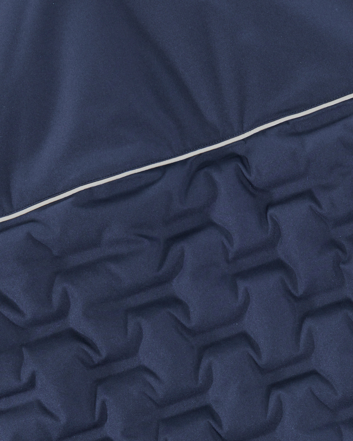 Close-up of a navy blue quilted fabric with a star-like pattern and a thin white piping detail running diagonally across the center.