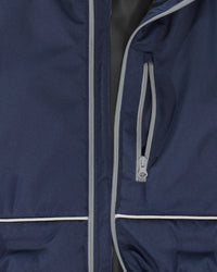Close-up of a navy blue jacket with light gray piping and a zippered pocket, showing the fabric texture and zipper details.