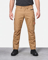 A model from the waist down wearing tan cargo work pants with black zippers and black work boots, set against a plain studio background.