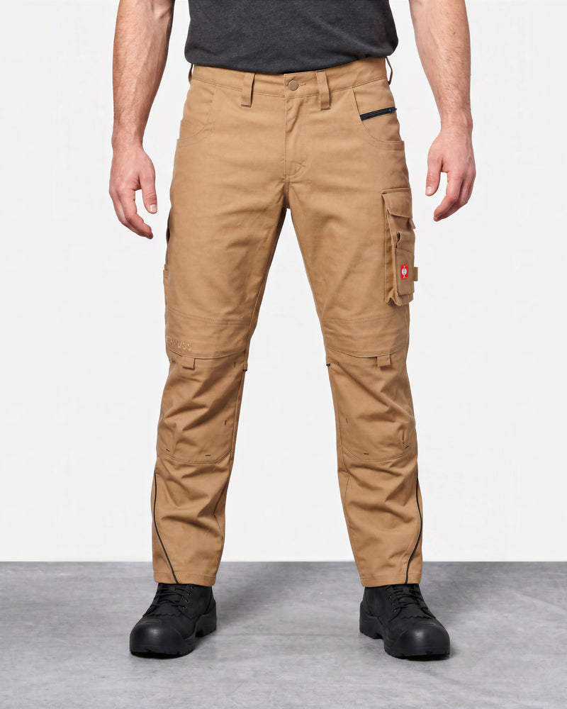 A model from the waist down wearing tan cargo work pants with black zippers and black work boots, set against a plain studio background.