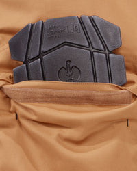 Close-up of a dark gray protective pad with embossed branding and logo, attached to a tan or camel-colored fabric garment.