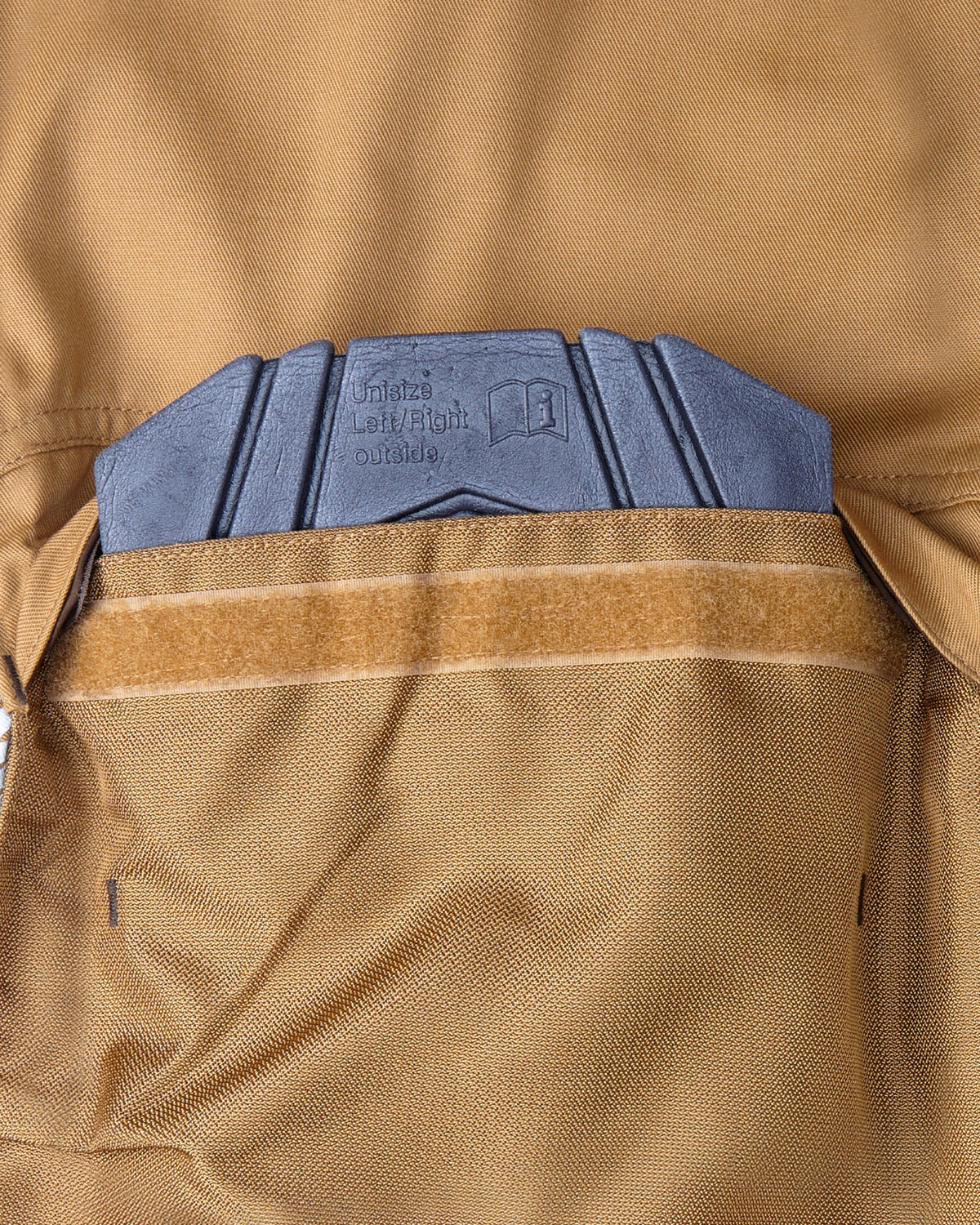 Close-up of a tan knee pad pocket with a hook-and-loop strap and a blue-gray textured pad visible at the top.