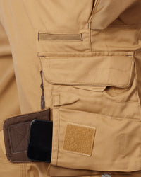 Close-up of a tan work shorts showing a side utility pocket with a brown zippered compartment holding a black smartphone, alongside a tan Velcro patch.