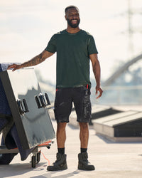 Engelbert Strauss e.s. motion ten shorts in oxid black in a lifestyle action view, highlighting the practical pocket access and durable workwear silhouette.