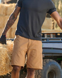 Engelbert Strauss e.s. iconic shorts in almond brown in an in-use workwear scene, showing the shorts worn during active movement and emphasizing comfort and mobility.