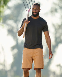 Engelbert Strauss e.s. iconic shorts in almond brown in a lifestyle action view, highlighting the practical pocket access and durable workwear silhouette.