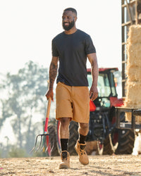Engelbert Strauss e.s. iconic shorts in almond brown in an outdoor-style lifestyle view, showing the shorts as part of a functional work outfit.