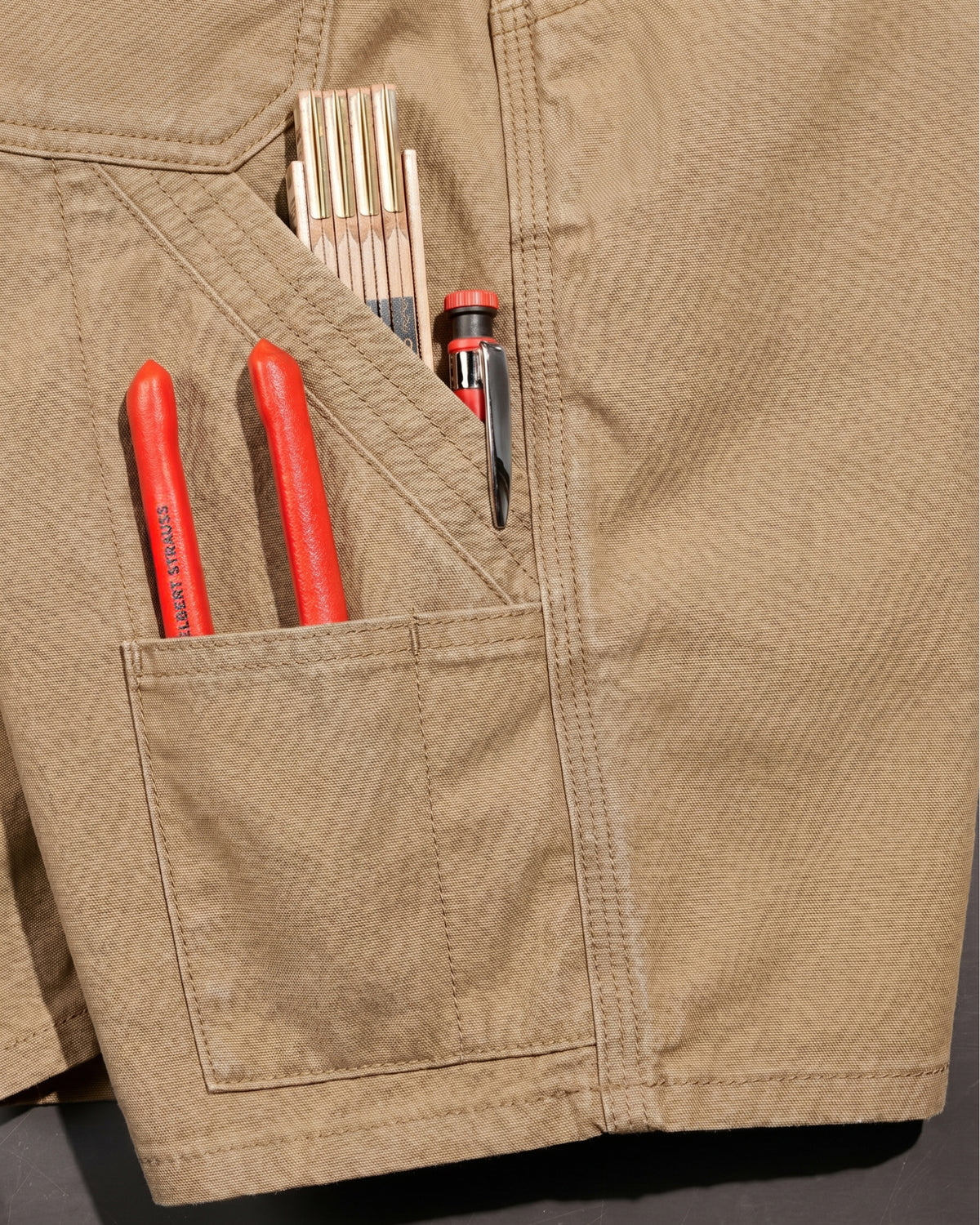 Close-up detail of Engelbert Strauss e.s. iconic shorts in almond brown, focusing on the utility pocket area, seams, and reinforced workwear construction.
