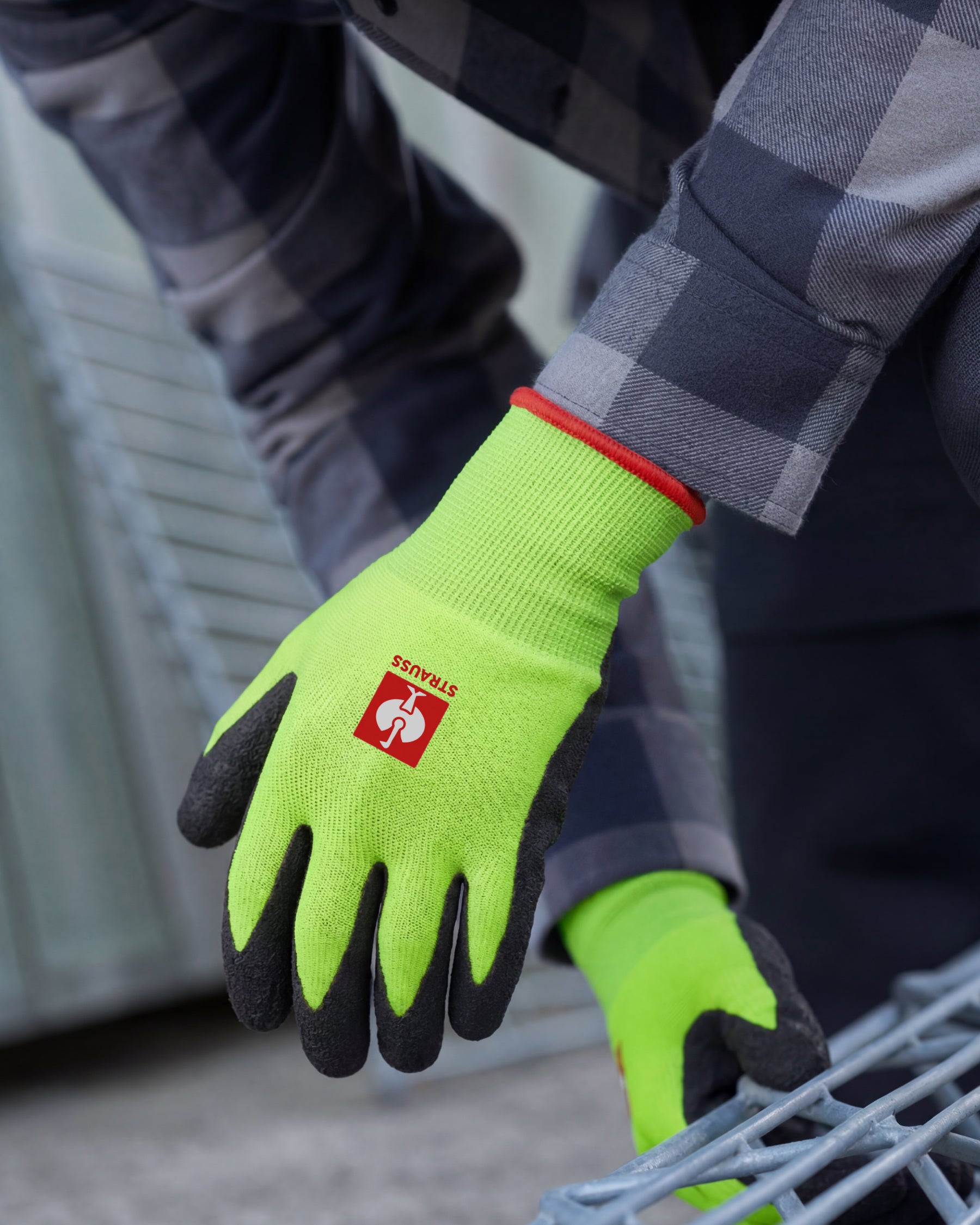 A worker wears neon green and black STRAUSS Senso-Grip latex knit gloves while gripping a hand tool at a workbench.