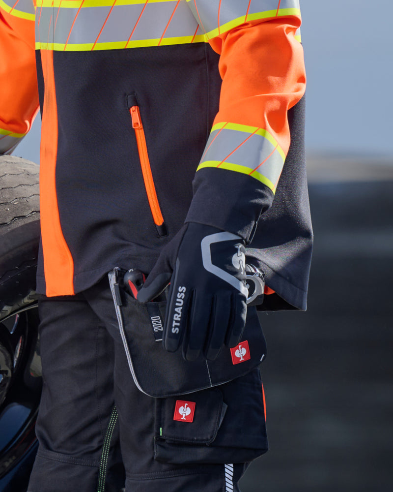 A worker wears black and basalt gray STRAUSS e.s.trail winter gloves while gripping a hand tool at a workbench.