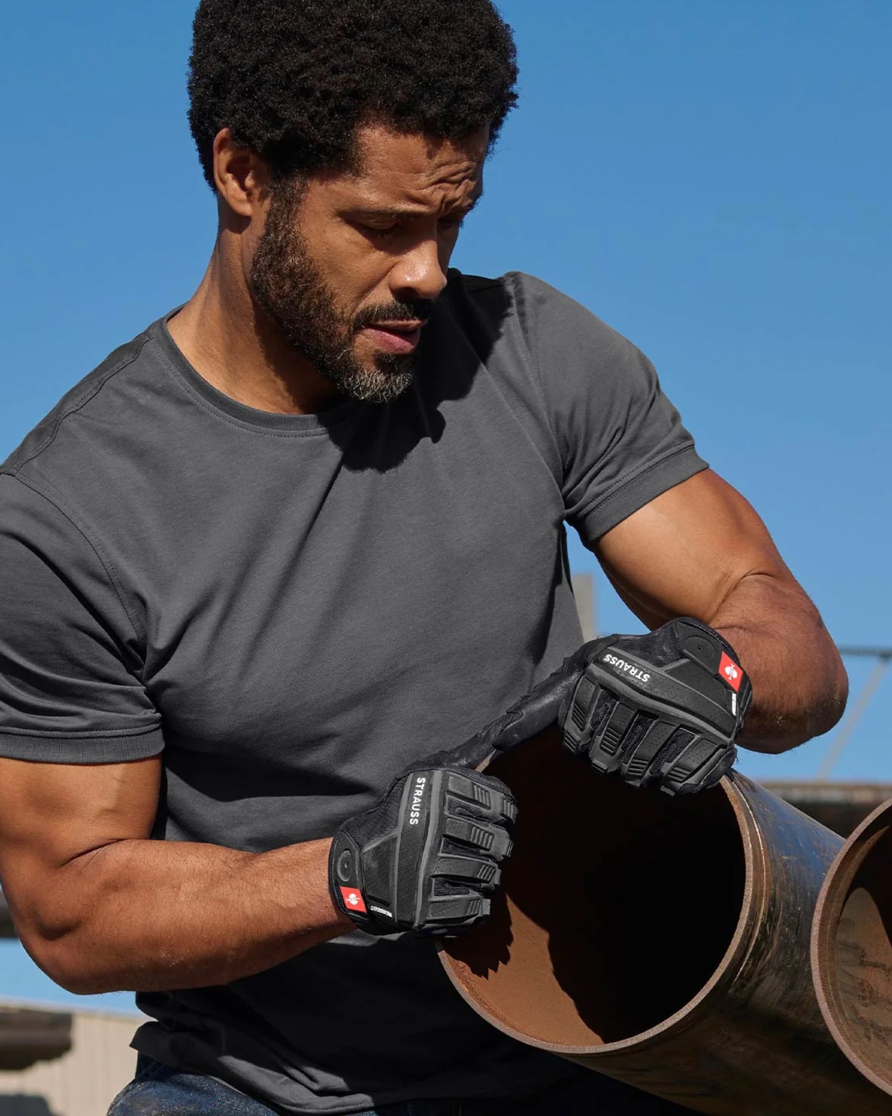 A worker in STRAUSS workwear uses black assembly protection gloves while handling jobsite materials.