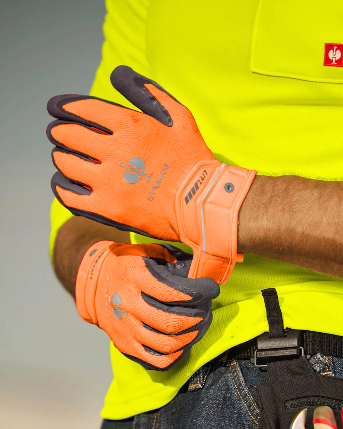 A worker wears neon orange and anthracite STRAUSS e.s.motion 24/7 hybrid gloves.