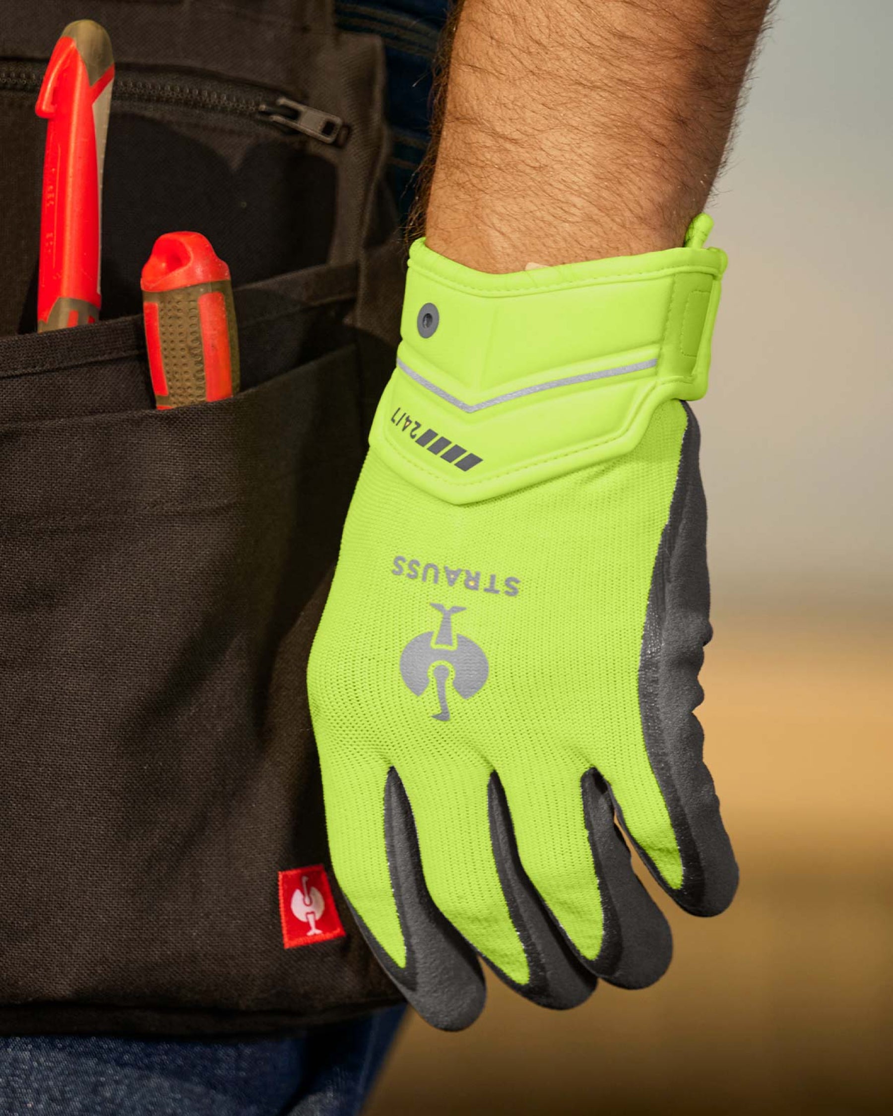 A close work scene shows neon yellow and anthracite STRAUSS e.s.motion 24/7 hybrid gloves protecting hands during a task.