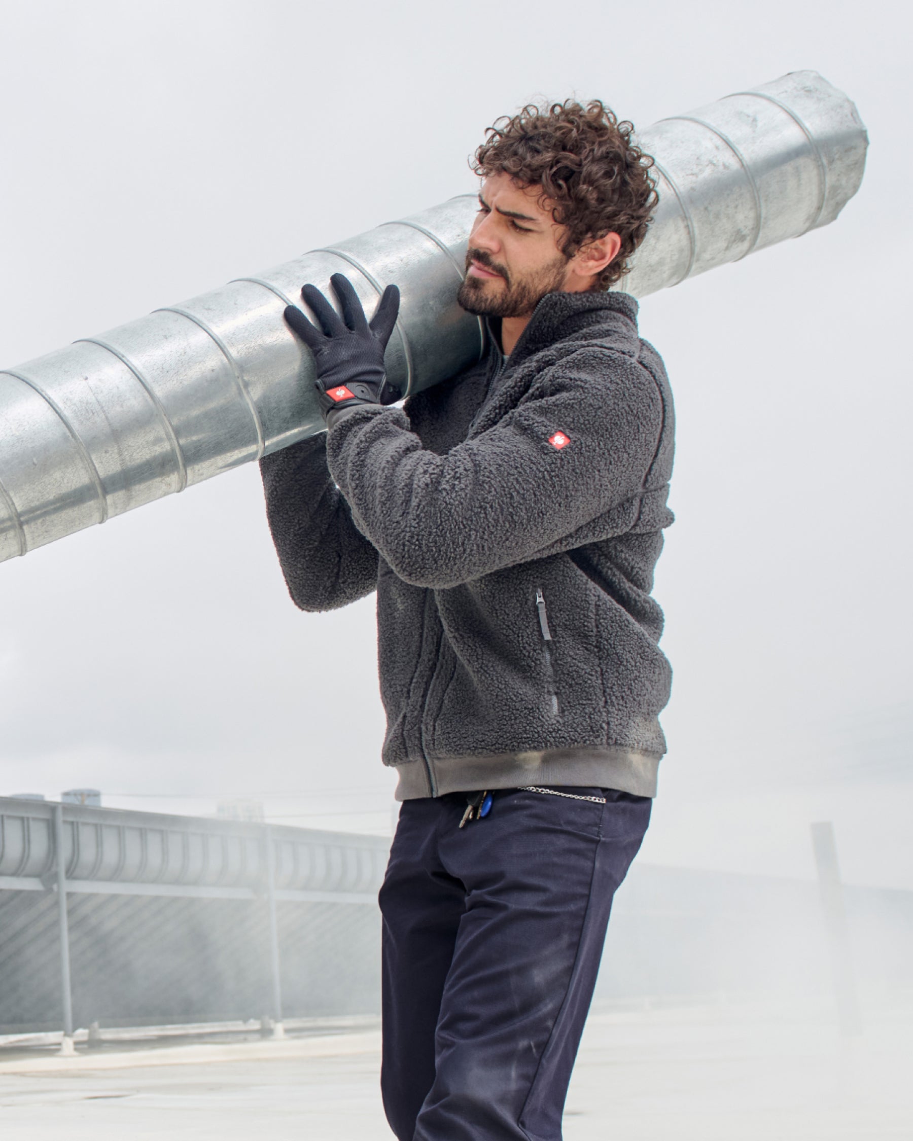 A worker wears black STRAUSS light assembly protection gloves while carrying materials.