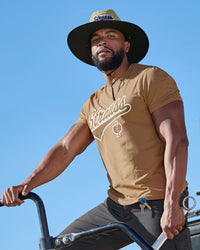 A model wears a light brown STRAUSS e.s.e:pic straw hat with a casual STRAUSS workwear outfit.