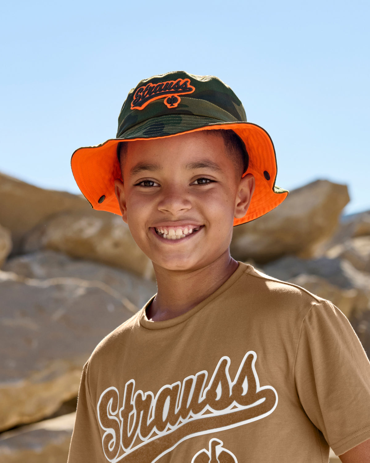 A model wears a camouflage STRAUSS kids' e.s.e:pic bucket hat with a casual STRAUSS workwear outfit.