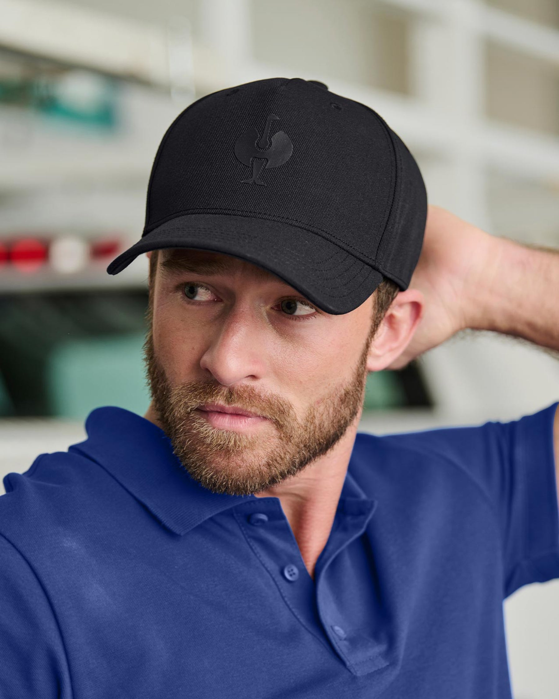A worker wears a black STRAUSS e.s.trail trucker hat with a work shirt and utility pants outdoors.