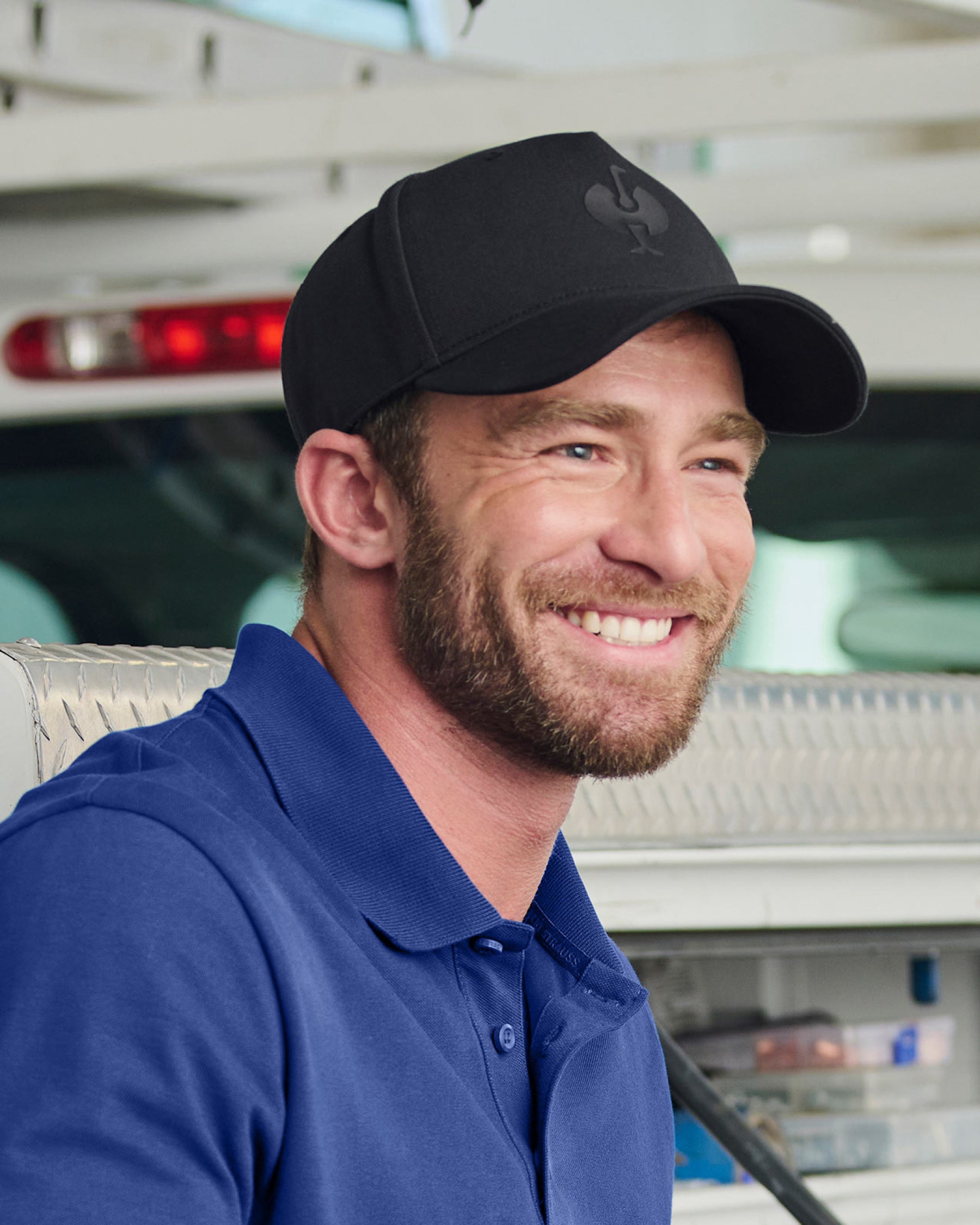 A model wears a black STRAUSS e.s.trail trucker hat with a casual STRAUSS workwear outfit.