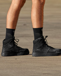 A person wears black and basalt gray STRAUSS e.s.trail pure all-season high-cut socks with work shoes in a casual product scene.