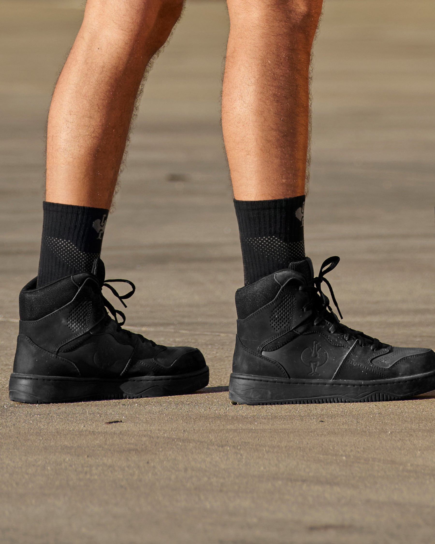 A person wears black and basalt gray STRAUSS e.s.trail pure all-season high-cut socks with work shoes in a casual product scene.