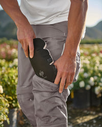 A worker kneels in STRAUSS work pants with black flex knee pads cushioning the knees.