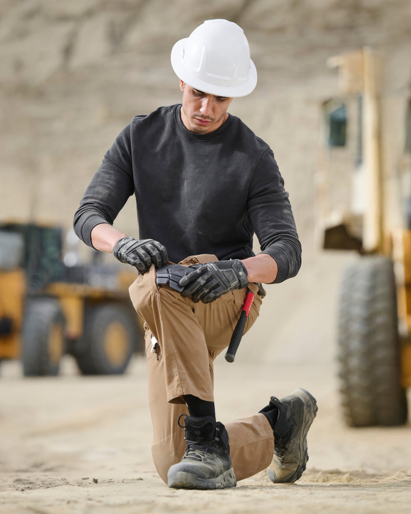 A worker kneels in STRAUSS work pants with graphite ergonomic knee pads cushioning the knees.