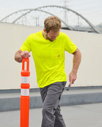 A worker wears the STRAUSS Enhanced Visibility Performance T-Shirt in neon yellow with work pants while handling materials at a jobsite