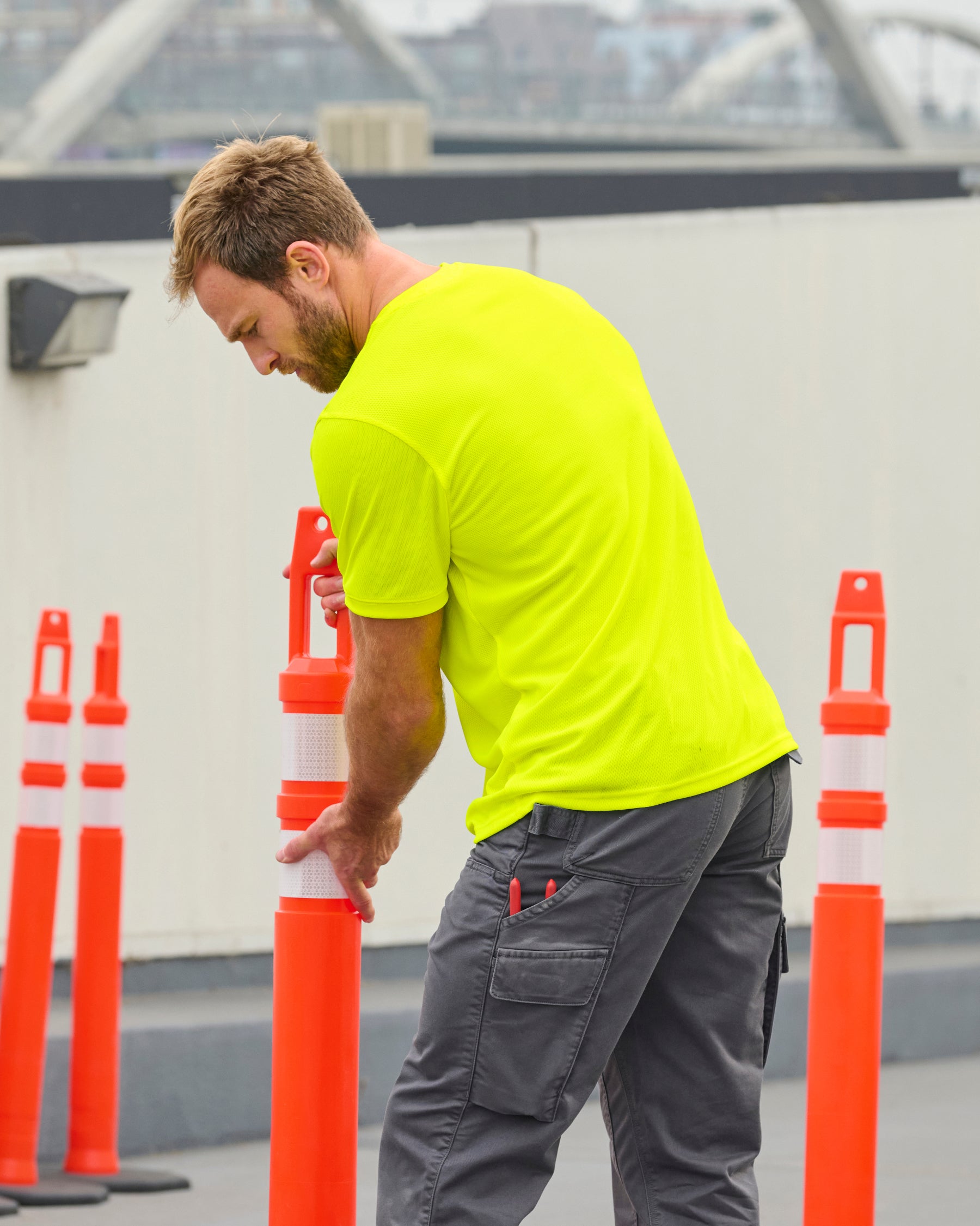 A worker wears the STRAUSS Enhanced Visibility Performance T-Shirt in neon yellow with work pants beside a work truck and jobsite gear