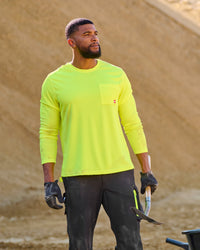 A worker wears the STRAUSS Enhanced Visibility Performance Long Sleeve Shirt in neon yellow with dark work pants near construction equipment