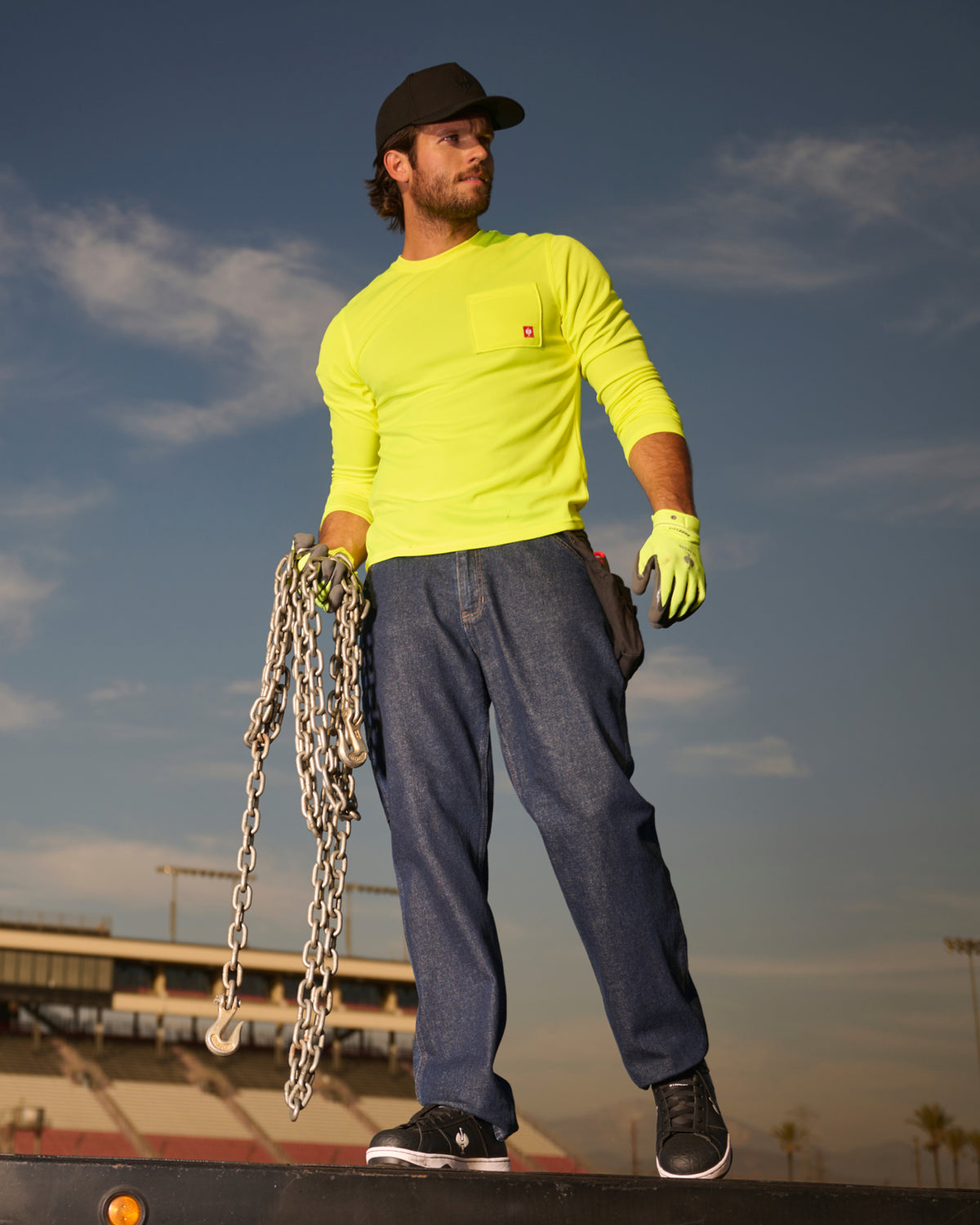 A worker wears the STRAUSS Enhanced Visibility Performance Long Sleeve Shirt in neon yellow with work pants while handling materials at a jobsite