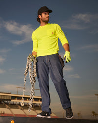 A worker wears the STRAUSS Enhanced Visibility Performance Long Sleeve Shirt in neon yellow with work pants while handling materials at a jobsite