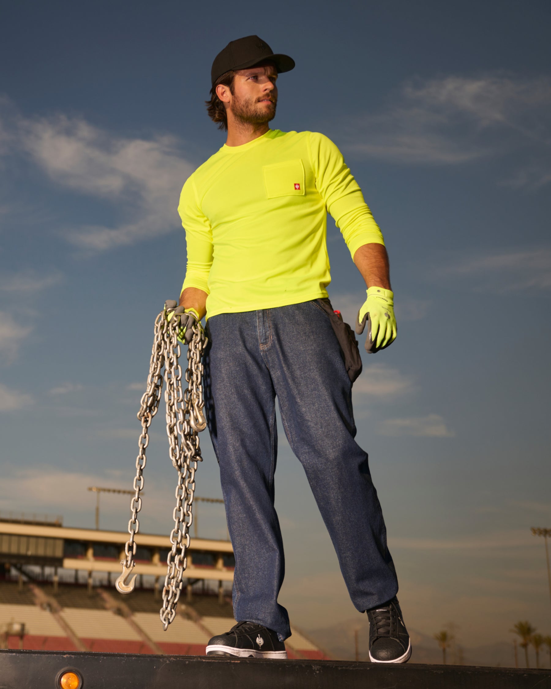 A worker wears the STRAUSS Enhanced Visibility Performance Long Sleeve Shirt in neon yellow with work pants while handling materials at a jobsite