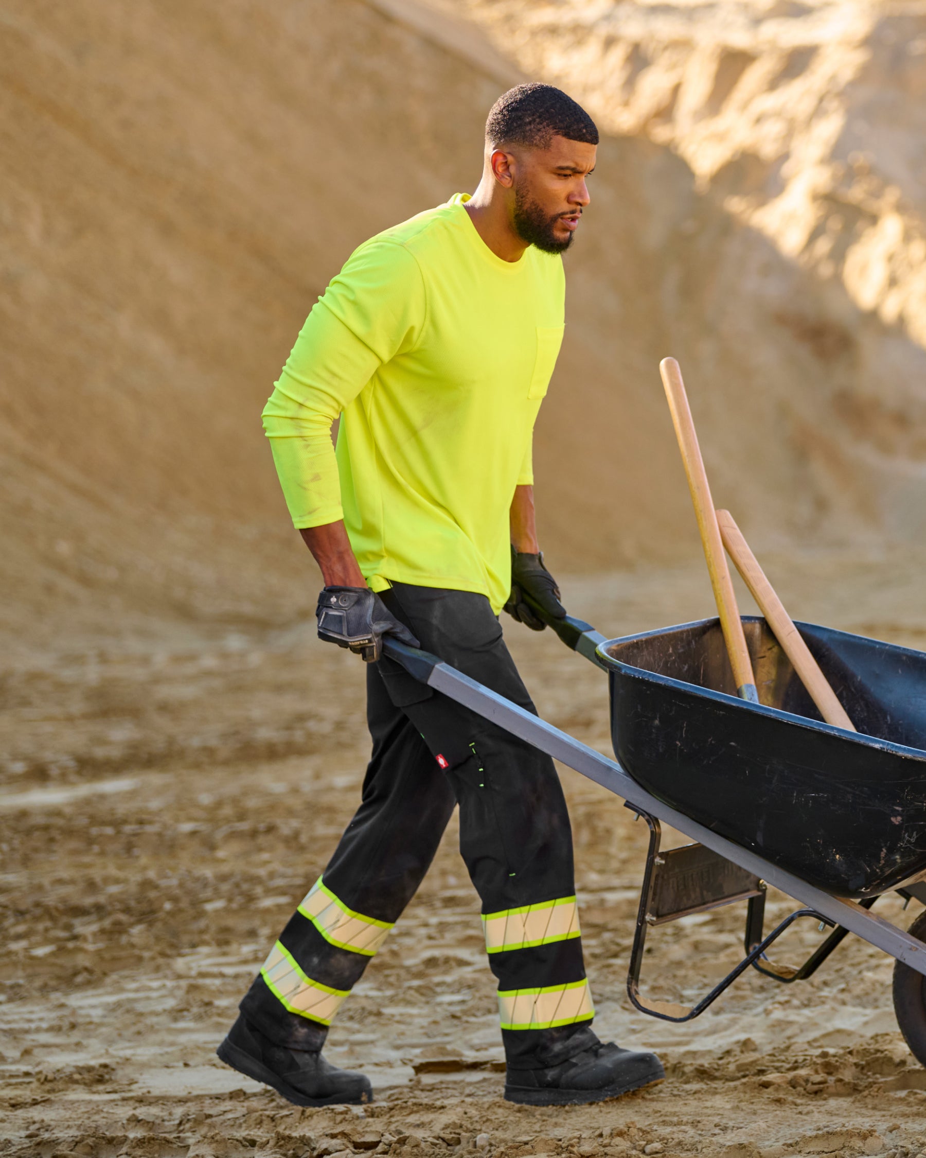 A worker wears the STRAUSS Enhanced Visibility Performance Long Sleeve Shirt in neon yellow with work pants beside a work truck and jobsite gear