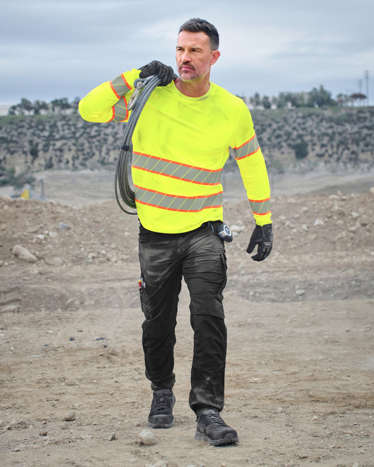 A worker wears the STRAUSS Class 2 High Visibility Long Sleeve Shirt in neon yellow with work pants while handling materials at a jobsite