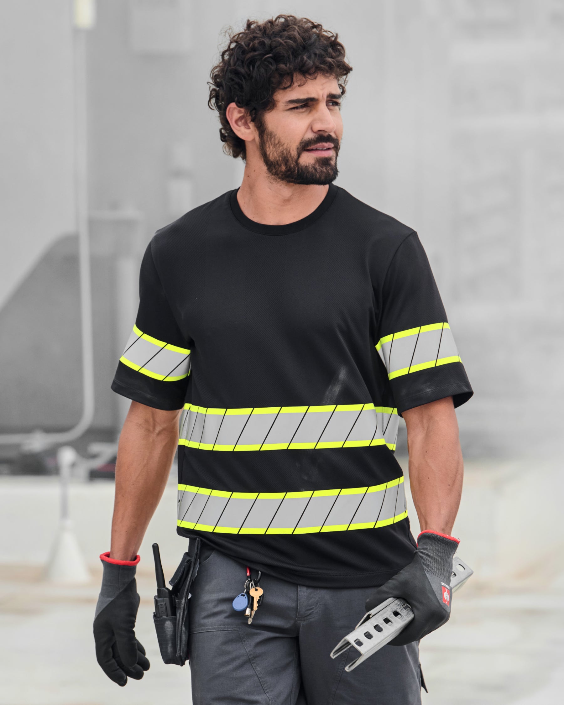 A worker wears the STRAUSS Enhanced Visibility T-Shirt in black with dark work pants near construction equipment