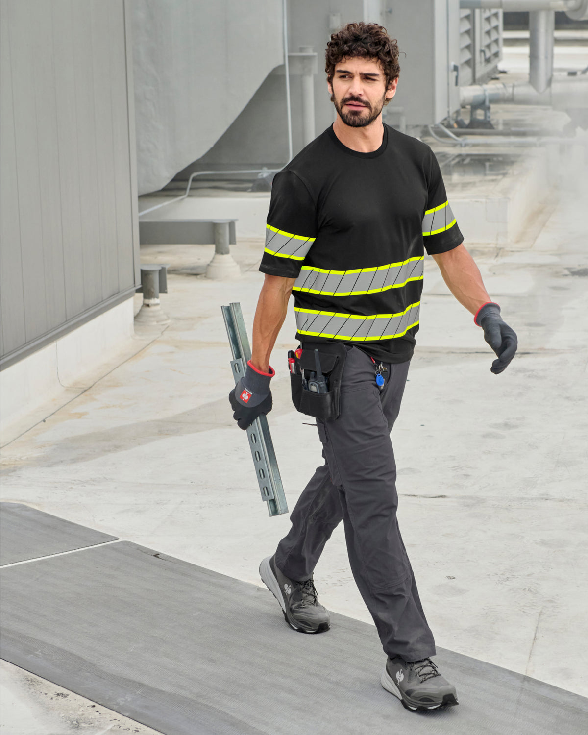 A worker wears the STRAUSS Enhanced Visibility T-Shirt in black with work pants while handling materials at a jobsite